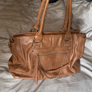 Ny Läderväska från Uhrika  - Läderväska från Uhrika, brun med gulddetaljer. Axelrem medföljer. Fack med dragkedja på båda utsidorna och flera fack på insidan. 