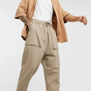 ASOS oversized beige byxor - Bekväma byxor från Asos Design i toppenskick! Knappt använda, och säljer då passformen inte funkade för mig. De är i storlek W30 L32, och går att dra åt så mycket man vill i midjan. De går till anklarna på mig som är 168cm!