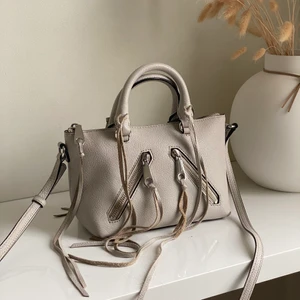 Rebecca Mikoff väska  - Ljusgrå supergullig väska med fransar från Rebecca Minkoff. Köpt i butiken i Los Angeles för något år sedan men kommer inte så mycket till användning längre. Använd men i bra skick ✨ köparen får stå för frakten eller mötas upp i Stockholm/Östermalmstorg!