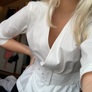 Vit blus från Nakd stl S - Jättesnygg vit blus från nakd med omlott där fram som man även kan knäppa upp vid av- och påtagning (se bild 3). Har 3/4 ärmar och avtagbart skärp i midjan. Säljer pågrund av att den inte kommer till användning tyvärr.