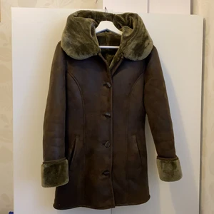 Vinterkappa - KONST-fårskinnsrock. Perfekt kortare kappa för vintern med en härlig luva fodret är i färgen grönbrun och jackan är brun. Mycket fint skick.