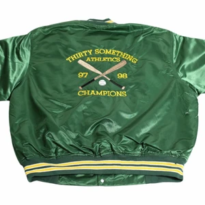 Stevie - Vintage Varsity Jacket  - En riktigt fin blank Nylon Varsity jacka i en cool pine green färg. Deb gjordes för basebollmästarna i 97/98. Den gjordes därför under 1990 -talet och är perfekt för 90-talets college aesthetic som är så svår att hitta. Deb är unik och sällsynt och dessutom i riktigt bra skick därför ett högre pris än resten av jackorna. Den var thriftad under tidigt 00-tal men aldrig använts.