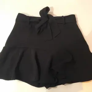 Svart kjol med knyte i midjan från Zara i storlek S.  Använd ett fåtal gånger men en är en söm som är lite öppen, går lätt att fixa genom att sy för hand. Säljer då den inte används längre. Vid leverans står köparen för kostnad för frakt o påse. 