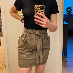 Paper bag-kjol från Acne - Fin armygrön sommarkjol från Acne. Skärp i midjan som går att byta ut och fickor på sidorna. Endast använd en gång, säljer den då den är lite stor i midjan för mig. För referens mäter jag 69-70 cm i midjan. 79% Bomull 21% siden.