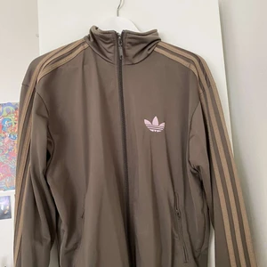 Adidas zip up - Skit snygg Brungrön adidas zip up med rosa logga. Tyvärr lite stor på mig men passar S/M/L. Unisex och ny skick👌🏼