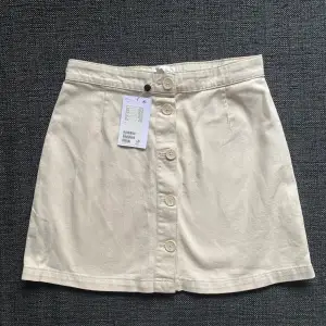 Oanvänd beige kjol från Monki stl 38  Säljer pga fel storlek Fint mönster på knapparna också :) 