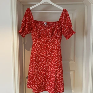 Jättefin sommarklänning i strl. 38 - En underbar röd sommarklänning i kort modell och med vita blommor. Märke- Bubbleroom. Storlek 38. Så fina detaljer med puffärmar och figursydd överdel. Smock i ryggen som gör att den sitter som en smäck! Använd enstaka gång. 