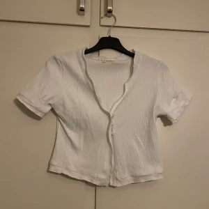 Topp  - Vit croppad topp, knappar framtill men inga som syns. Liten i storleken