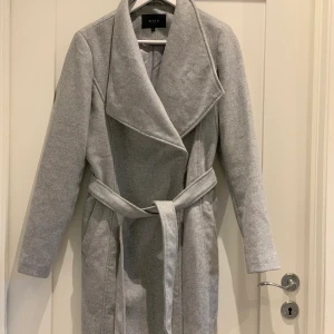 Vila Ljusgrå Kappa strl L - Nästan helt oanvänd kappa i strl L. Mkt fint skick, bara hängt i garderoben senaste året. 
