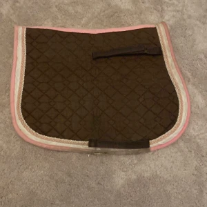 Brunt/rosa schabrak - Jag säljer mitt bruna schabrak med rosa detaljer! Använt en del men längesedan det användes, det har legat i ett skåp i över ett år och känner att det borde komma till användning snart!💗Lite slitet vid sadelgjorden men det kommer inte synas med sadel på!