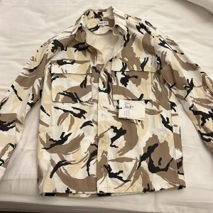 Kamouflerad Kenzo overshirt  - Hej säljer nu min Kenzo overshirt som jag fick i present. Plagget är köpt på Johnells i Uppsala, säljer då den inte används och då det inte passar min stil. Plagget är använt 1-2 ggr och är i utmärkt skick. Prislapp finns med.