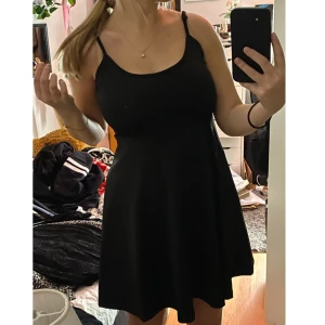 Svart klockad klänning - En svart enkel klänning med klockad kjol. Överdelen är som ett v-ringat linne med justerbara axelband. Sitter skönt. Ganska tjockt tyg. 