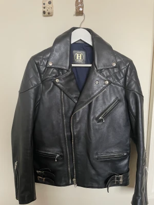 Svart läderjacka (biker) - Fin svart läderjacka biker-modell i kalvskinn. Skräddarsydd i HongKong. Ser L men asiatisk storlek. Passar snarare stl 46/S. Sitter för tight på mig som har 48/M. Lite sprucken i insidan/fodret. Går att fixa till enkelt hos skräddare. I övrigt fint skick.