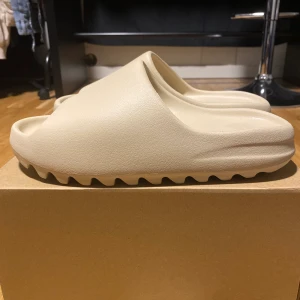 Yeezy slide BONE - Yeezy slide BONE storlek 44,5 passar även alla storlekar som 41, 42, 43. Skriv ifall du vill ha mer bilder. HELT ÄKTA YEEZY SLIDE. Dom är beige vita. HELT NYA ALDRIG ANVÄNDA.