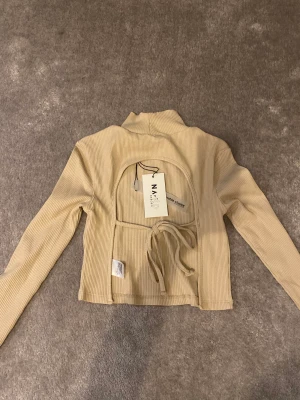 Topp med öppen rygg - Säljer denna beige tröja Med öppen rygg från NAKD💕 helt oanvänd