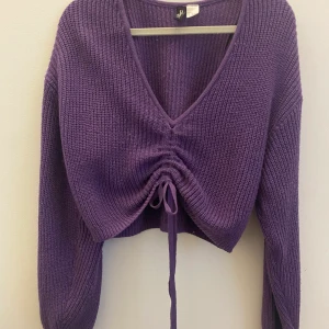 Lila, stickad tröja från HM - Croppad, stickad tröja från HM. Man kan avgöra hur högt upp tröjan ska sitta på magen med hjälp av ett snöre (visas på andra bilden). Använt några få gånger.