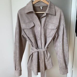 Skjortjacka/shacket - Skjortjacka från NLY Trend i storlek 34, knappt använd. Färgen är åt mauve-hållet (grå/lila/rosa), och materialet är i suede. Fickor på brösten samt sidofickor för händerna. Stängs med knappar och skärp🤗
