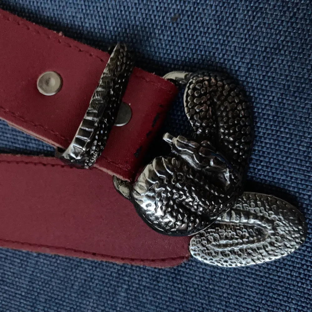 litet bälte i rött läder med buckle i metall i form av orm . Accessoarer.
