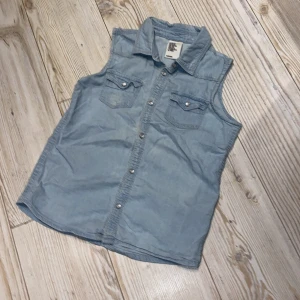 Jean-linne - Ett enkelt ljusblått jeans-linne med knappar och 2 små fickor, gott skick