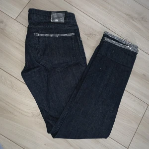 Mörka jeans med glitterdetaljer - Mörkblåa jeans med glitter på bland annat fickan. Se bild. De har sytts upp men bör gå att sprätta upp ifall det önskas. 