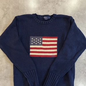 Polo Ralph Lauren Flag Crewneck - Polo Ralph Lauren Stickad tröja, Väldigt fin kvalite och skick The Iconic Flag Jumper Flag Sweater / Crewneck Storlek L Nypris 4100kr Nagy Färg Denna är en vintage modell