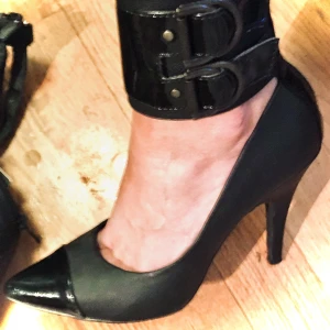 Högklackade Lack/Skinn skor - Sjukt snygga oanvända skor, strl 38 nypris 399. Dragkedja baktill. Vackert lack och spännen runt ankeln. Resten skinn och tåspets i lack. Kan tyvärr inte gå i högklackat längre och har därför aldrig använt dom..😞