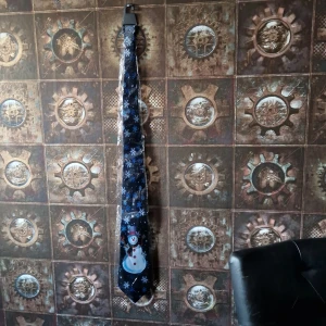 Snögube - En oanvänd jul slips med snö fligor och en snögube lägst ner .svart bakgrund vita och blå snöflingor samt snögube med hat o halsduk .frakt till komer 