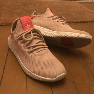 Adidas Pharell Williams i Beige - Ett par riktigt bekväma och snygga Adidas Pharell Williams skor i färgen beige. Har använt de 2 gånger och är så gott som nya.  Är i storlek 38 2/3. Svårt att få tag på de här skorna.                                                NYPRIS: 900kr