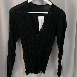 Krinklad svart blus.  - Detta är en krinklad svart blus som är i ett lite mer genomskinligt material från Gina Tricot. I storlek S och den är oanvänd. 
