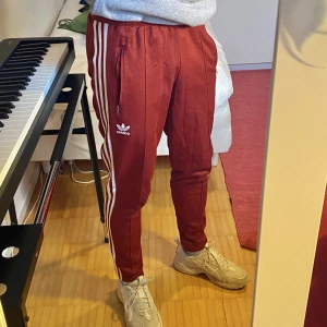 Röda adidas byxor  - Fint skick röda byxor, trefoil märket på ena sidan. Säljer för att de blivit för små. Frakt står köparen för. Nypris 699 kr