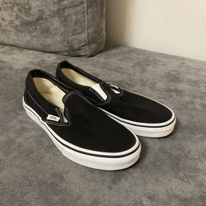 Svarta vans - Classic slip-on shoes från Vans, storlek 38,5. Innermått 24,5cm. Använda en gång. Säljer då de inte passade. Nypris 749kr