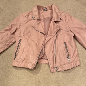 Skinnjacka  - Rosa skinnjacka. Silver blixtlås. Det står två initialer i nacken så den blir billigare. 