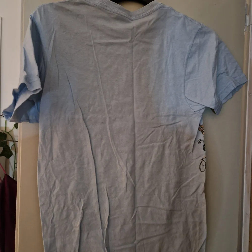 Ljusblå tshirt med tryck på i storlek M. Trycket är slitet, osäker om det är designen eller bara slitet.. T-shirts.
