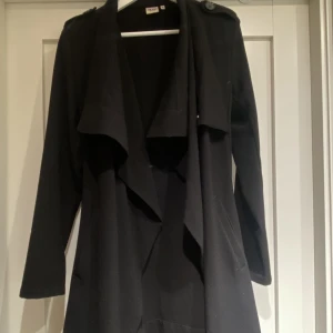 Svart vårkappa  - Svart vårkappa med fint fall från Object fashion. Med axelvaddar. Längd strax under knäna. Storlek M. 
