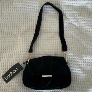 Oanvänd väska boohoo  - Oanvänd väska från boohoo i sammet. Ca 20 cm på bredden. Aldrig använd men kom med små märken på spännet, se bild tre. 