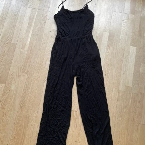 Svart jumpsuit ifrån H&M - En svart jumpsuit i storlek S ifrån H&M. Otroligt svalt material och lite tunnare band. Längden är 154 cm och fler bilder kan fås! Kan skickas