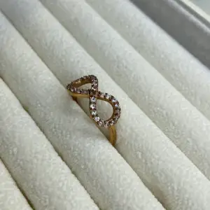 En ring i rosefärg med glittriga stenar, ringen har en form i oändlighetstecknet. Fråga om storlek i cm vid intresse 🥰Men skulle säga small- medium ❣️ Fint skick FRAKT 12 KR