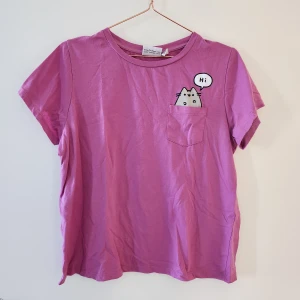Pusheen-t-shirt - Söt t-shirt där Pusheen tittar ut ur fickan! Det står strl 44 men är högst som en 38! Hör av dig om du har frågor!