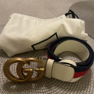 Gucci Skärp.  - Äkta GG gucci-skärp i mässing. Köpt i milano för 1 år sedan. Vit läder och färg vit/röd/blå. Inte användt det mer än 3 gånger och är därför i butiks-skick. Köpte i butik för 3000. Är 85 cm långt. Inget kvitto kvar men kommer med original dustbag.