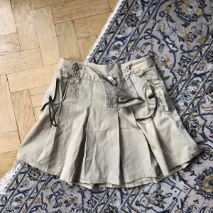 Mini-kjol, Cargokjol - Plisserad ”cargo”-kjol från Hunkydory! I tjock bomull, bra kvalitet. Går att öppna på två sidor fram med knappar och dragkedjor! Har även söta små fickor med läderremmar som stänger till ☺️ska förm. hänga på höfterna men funkar nog perfekt i midjan på M! 💕