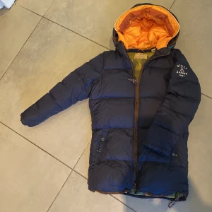 Dun jacka i toppen skick  - Dun jacka från märket scotch and soda! Använd några gånger, så i toppen skick!  Den oranga luvan går att knäppa av. 