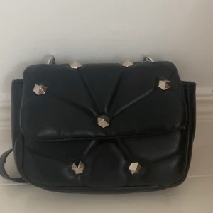 svart nitväska - Säljer denna trendiga svarta nitväskan. Köpt i mars, använd ungefär 3ggr. 😁 Inga defekter, köptes för 180kr så säljer för 90kr + frakt💖 Den har silvriga detaljer och det är även en ficka i. TRYCK INTE PÅ KÖP NU, SKRIV ISTÄLLET🥰