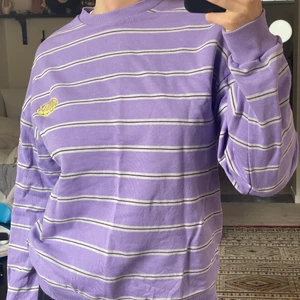 Lila Collegetröja  - Lila randig collegetröja från junkyard! Märker är multiverse och färgerna går i lila, vitt, mörklila och gul logga! Felfritt skick!