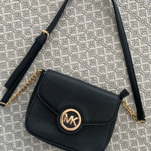 Michael kors väska  - säljer en fin liten Michael kors väska som är perfekt nu till våren och sommaren som är en fin detalj till outfiten. Den är svart med guldiga detaljer