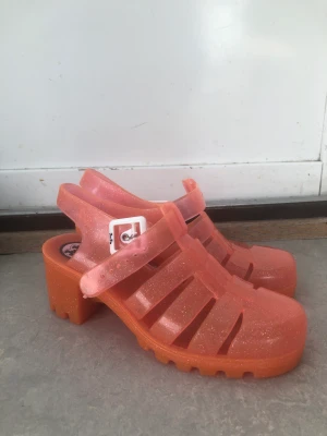 JuJu glittriga klackskor plastskor  - Jättecoola klackskor i plast från Brittiska JuJu. Rosa med glitter i! Fina till fest eller vardag, med eller utan strumpor i. Storlek:37