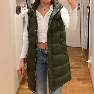 Puffer väst lång - Superfin lång dunväst i en kakigrön färg (nyskick). Är köpt på gekås, fick tyvärr aldrig användning för den så nu säljer jag den. Storlek XS. Jag är 161 cm lång!