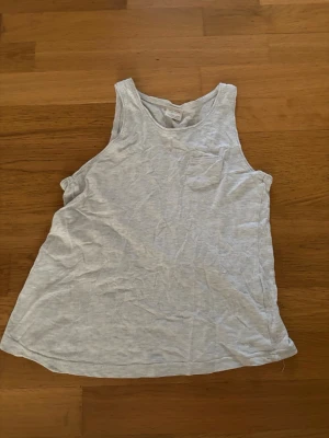 Ljusgrått linne från Zara Girls - Linne i ljusgrå bomull från Zara Girls. Modellen är ärmlös med rund halsringning och liten bröstficka. Perfekt för varma dagar och enkel att matcha med jeans eller shorts.