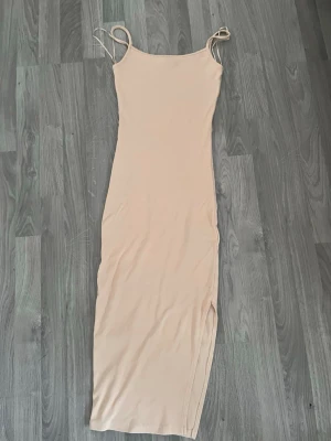 Beige ribbad långklänning - Trendig beige långklänning med smala axelband och ribbad struktur. Klänningen har en slits på sidan för extra stilpoäng och är figurnära i modellen. Perfekt för dig som gillar minimalistisk och clean look.