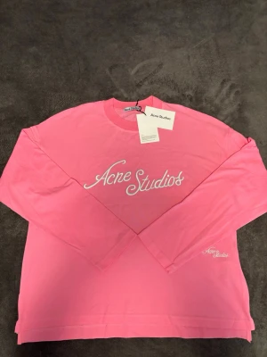 Rosa långärmad tröja Acne Studios - Snygg rosa långärmad topp från Acne Studios med vit broderad logga framtill och på ärmen. Oversized passform och rund halsringning. Ganska unik modell då inte många har den. Skricka gärna bud💕🙏🏻