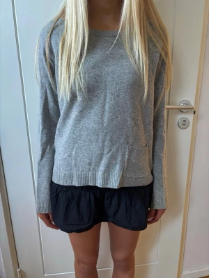 Stickad kaschmir och ulltröja - Mysig grå stickad tröja med rund hals och en liten ficka framtill. Tröjan har långa ärmar och ribbade muddar vid hals, ärmslut och nederkant. Vet ej storlek men passar S. Materialet är ull och kaschmir. Märket är Marc o’polo.